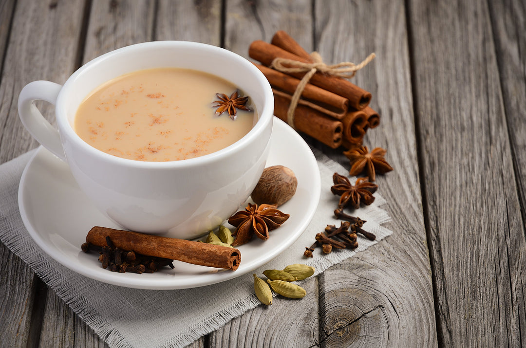 weiße Teetasse gefüllt mit Chai Tee, drumherum Zimtstangen