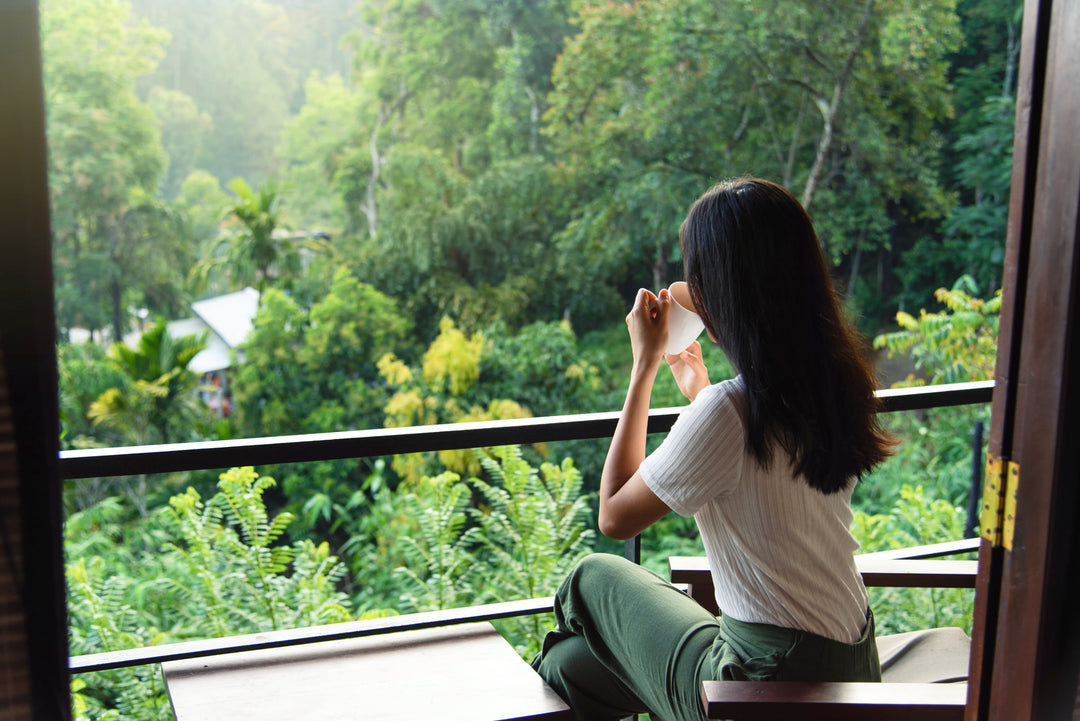 Frau mit einer Tasse Tee auf dem Balkon und Blick aufs Grüne